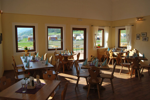 Comedor soleado en Camping Bella Austria, Stiria, con sillas de madera y vistas al área de caravanas.