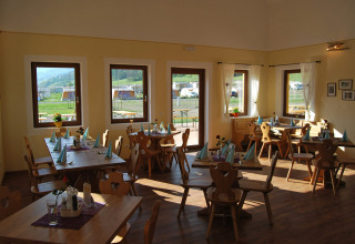 Sunny dining room at Camping Bella Austria in Styria with wooden chairs, tables, and views of the campsite.