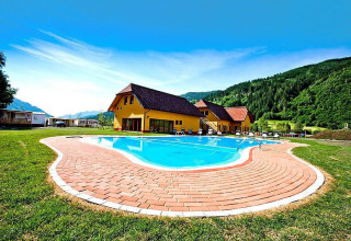 Piscina esterna presso Camping Bella Austria, circondata da verdi colline e case con tetti rossi.
