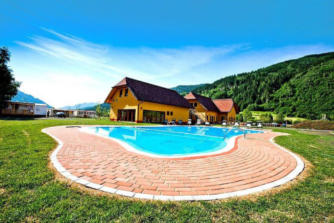 Piscina esterna presso Camping Bella Austria, circondata da verdi colline e case con tetti rossi.