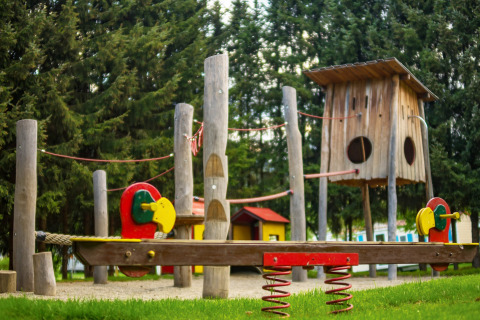 Parco giochi con altalene in legno e strutture colorate al Camping Bella Austria in Stiria, Austria, tra gli alberi.