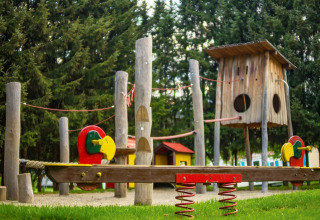 Parco giochi con altalene in legno e strutture colorate al Camping Bella Austria in Stiria, Austria, tra gli alberi.