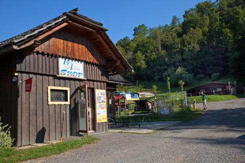 Wooden shop building at Camping Bella Austria holiday park in Styria, Austria, with people and green hills.