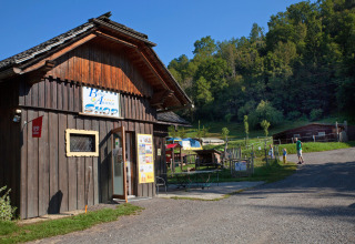 Wooden shop building at Camping Bella Austria holiday park in Styria, Austria, with people and green hills.