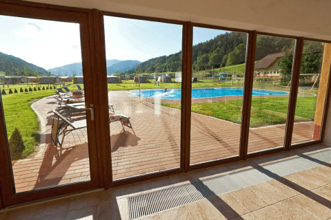 Vista a través de grandes ventanales al área de la piscina y colinas en Camping Bella Austria en Estiria.