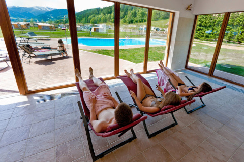 Ospiti rilassati su lettini interni con vista sulla piscina e montagne al Camping Bella Austria in Stiria, Austria.