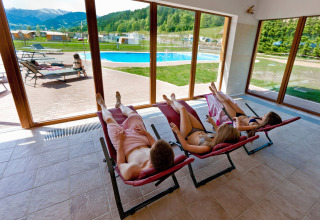 Huéspedes descansan en tumbonas interiores con vistas a la piscina y montañas en Camping Bella Austria, Estiria.