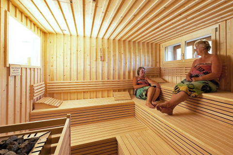 Two women relaxing inside a spacious, wooden sauna at Camping Bella Austria holiday park in Styria, Austria.