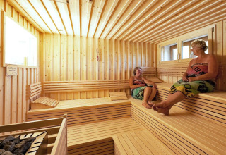 Twee vrouwen ontspannen zich in een ruime houten sauna bij Camping Bella Austria in Steiermarken, Oostenrijk.