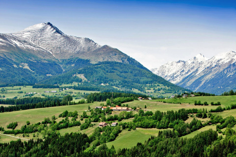 Paesaggio montano vicino a St. Peter am Kammersberg, Austria, con colline verdi e cime innevate.
