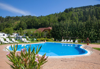 Outdoor pool with sun loungers, lush green forest, and mountains at Camping Bella Austria, Styria, Austria.