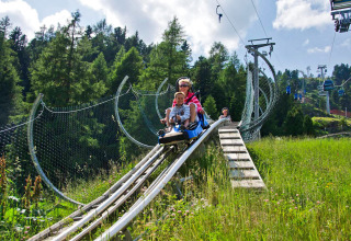 Dos personas viajan en una montaña rusa alpina en Camping Bella Austria, rodeados de naturaleza y bosque.