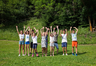 En gruppe børn løfter hænderne og smiler på en grøn mark ved Camping Bella Austria i Stiermarken, Østrig.