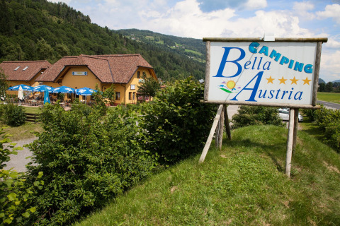 Sign for Camping Bella Austria beside a holiday park with a restaurant in green hills of Styria, Austria.