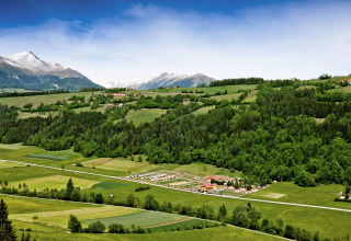Vista panoramica del campeggio Bella Austria in Stiria, con colline verdi e montagne innevate sullo sfondo.