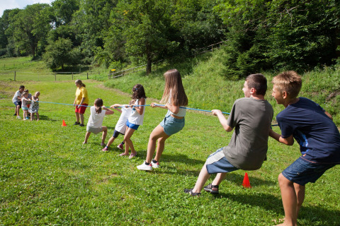 Niños jugando a tirar de la cuerda sobre césped verde en verano en Camping Bella Austria en Estiria, Austria.