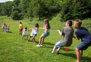 Children playing tug-of-war on a green field in summer at Camping Bella Austria holiday park in Styria, Austria.