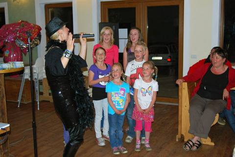 Gruppo di bambini con una cantante durante una serata di intrattenimento al Camping Bella Austria in Stiria.