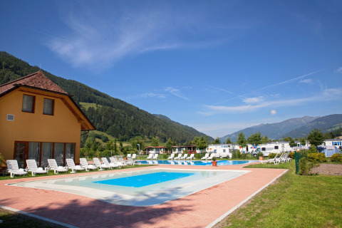 Piscina e lettini presso il Camping Bella Austria in Stiria, Austria, con sfondo di montagne verdi.