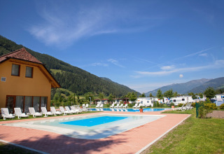 Piscina e lettini presso il Camping Bella Austria in Stiria, Austria, con sfondo di montagne verdi.