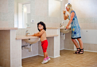 A child and a woman brush their teeth together in a bathroom at Camping Bella Austria holiday park.