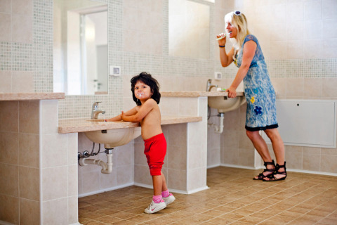 A child and a woman brush their teeth together in a bathroom at Camping Bella Austria holiday park.