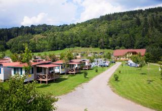 Camping Bella Austria holiday park in Styria with mobile homes, green fields and forested hills in the background.