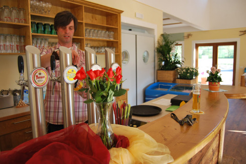 Bartender pours beer behind the bar at Camping Bella Austria, Styria, Austria, with flowers on the counter.