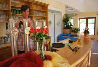 Bartender pours beer behind the bar at Camping Bella Austria, Styria, Austria, with flowers on the counter.