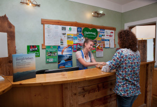 Receptioniste verwelkomt gast op Camping Bella Austria vakantiepark in Steiermark, Oostenrijk.