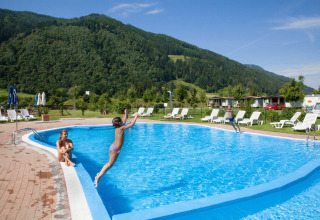 Bambini saltano in piscina circondati da sdraio e montagne al Camping Bella Austria, Stiria, Austria.