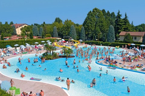 Persone si divertono in una grande piscina con scivolo al Camping Bella Italia, parco vacanze in Veneto, Italia.