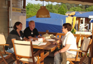 Two campsite staff members talking to a guest at the information desk at Camping Bella Italia, Veneto, Italy.