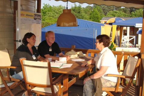 Two campsite staff members talking to a guest at the information desk at Camping Bella Italia, Veneto, Italy.