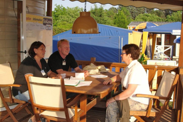 Two campsite staff members talking to a guest at the information desk at Camping Bella Italia, Veneto, Italy.
