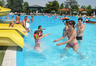 Famiglie si divertono in piscina e sugli scivoli gialli al Camping Bella Italia, parco vacanze in Veneto, Italia.