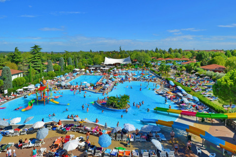 Large pool area with waterslides and sunbeds at Camping Bella Italia holiday park in Veneto, Italy, crowded.