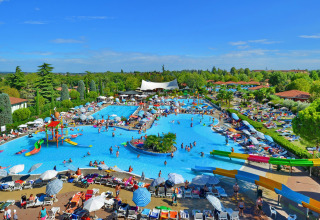 Stort poolområde med vandrutsjebaner og solsenge på Camping Bella Italia i Veneto, Italien, fyldt med gæster.