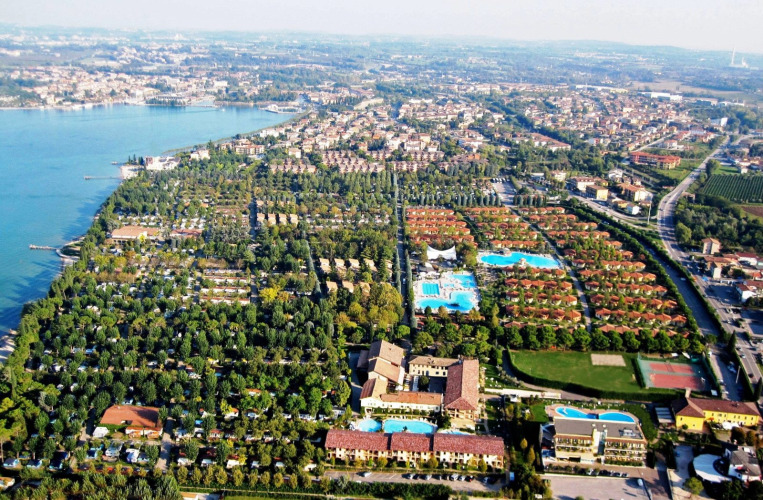 Aerial view of Camping Bella Italia holiday park in Veneto, Italy, featuring pools, trees, and lakefront scenery.