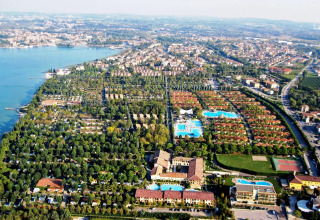 Vista aérea del Camping Bella Italia en Veneto, Italia, mostrando piscinas, vegetación y el lago cercano.