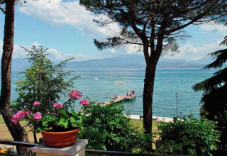View of the lake from Camping Bella Italia in Veneto, Italy, with flowers, trees, pier, and boats.