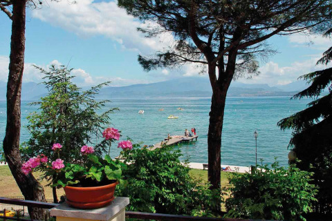 Vista dal Camping Bella Italia in Veneto, Italia, sul lago con fiori, alberi, pontile e barche.