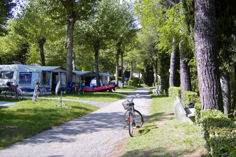 Zona de camping con tiendas, caravanas, bicicletas y árboles en Camping Bella Italia, Véneto, Italia.