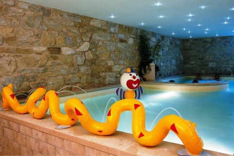 Piscina interior con paredes de piedra, fuente de agua en forma de serpiente y payaso en Camping Bella Italia.