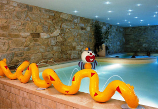 Indendørs poolområde med stenvægge, farverig slangevandfontæne og klovnefigur på Camping Bella Italia.