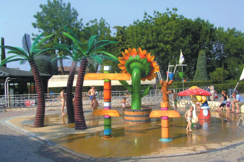 Niños se divierten en una colorida zona de juegos acuáticos en Camping Bella Italia, parque vacacional en Italia.