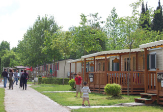 Visitantes pasean junto a casas móviles y zonas verdes en Camping Bella Italia, Veneto, Italia, en un día soleado.