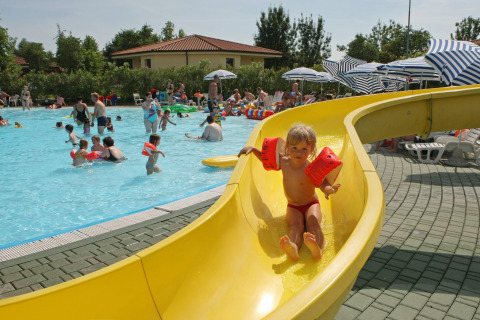 Niños jugando en una piscina con tobogán en Camping Bella Italia, un parque vacacional en Véneto, Italia.