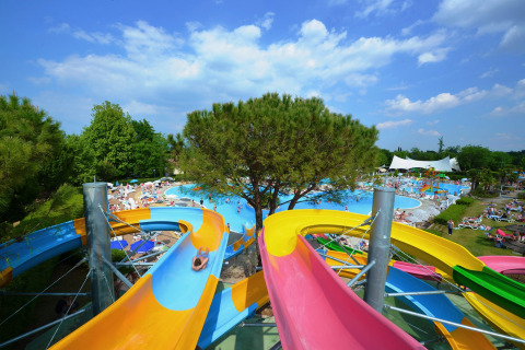 Toboganes de agua coloridos desembocan en la piscina principal de Camping Bella Italia en Veneto, Italia, en verano.