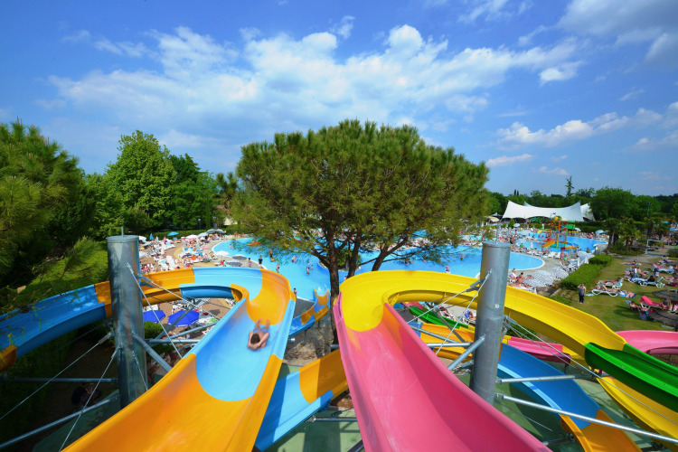 Colorful water slides lead to a pool area at Camping Bella Italia holiday park in Veneto, Italy, on a sunny day.